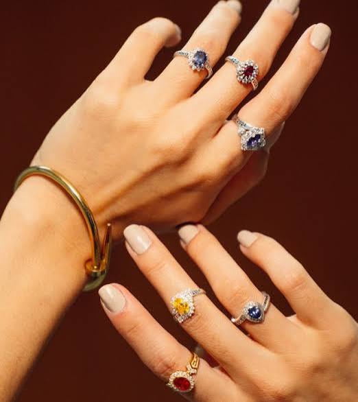 Manos con anillos de piedras de colores y una pulsera dorada